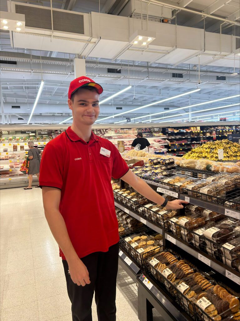 Jakob placing his left hand on a package of displayed cookies at inclusive employer Coles store