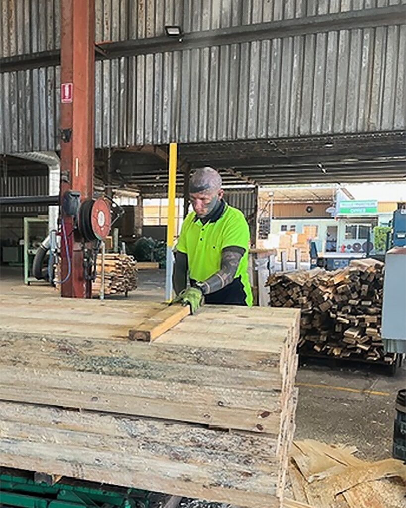 Matthew is working with a large wooden piece supported by a stack of other large wooden pieces.