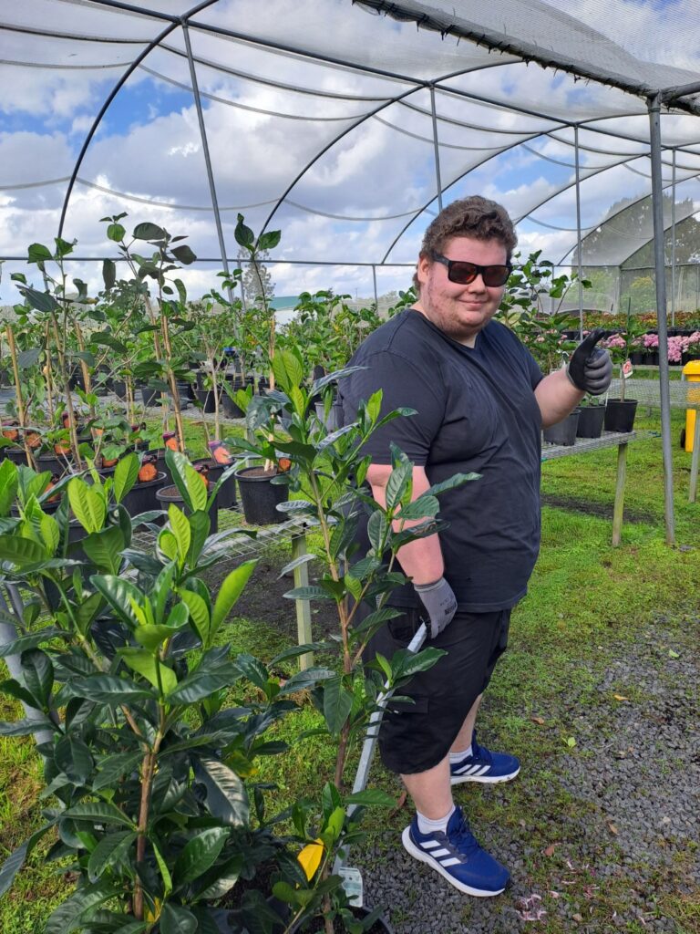 Robbie with his left thumb up and sunglasses in the nursery smiling at camera during his first work experience.