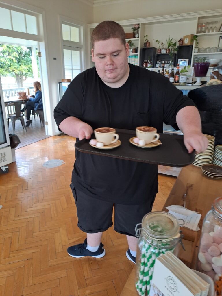 Robbie concentrated carrying a carry tray with two cups of coffee, looking at them during his work experience.