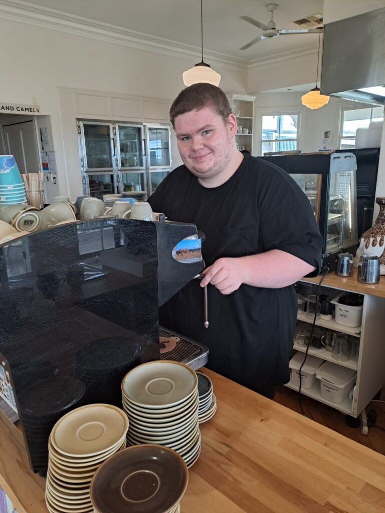 Robbie in front of the espresso machine smiling and looking at the camera.