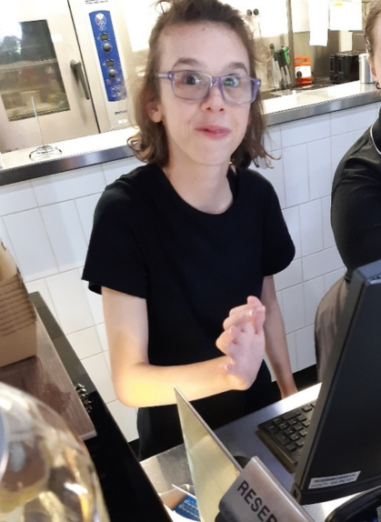 Rhiannon smiling at the camera while working at the cashier during her work experience, an employment opportunity for teenagers with disability