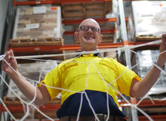 Supported Employee Kevin holding a net with both hands while smiling at the camera.